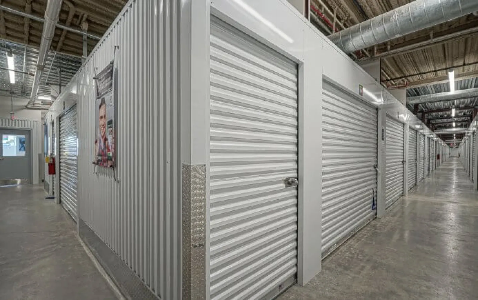 Interior view of a self storage facility with rows of closed metal roll-up doors and a concrete floor.
