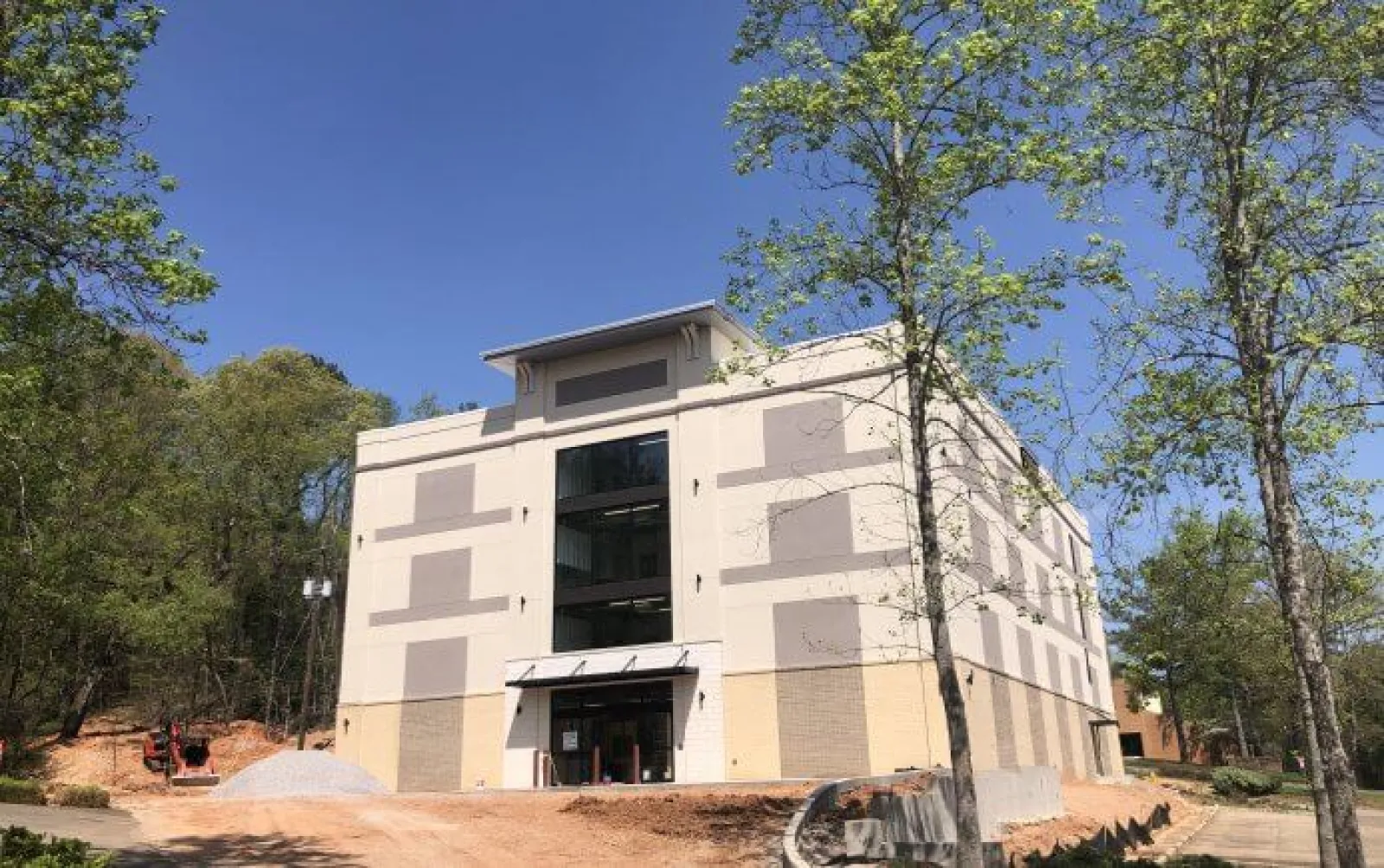 Newly constructed beige commercial building surrounded by trees under a clear blue sky.
