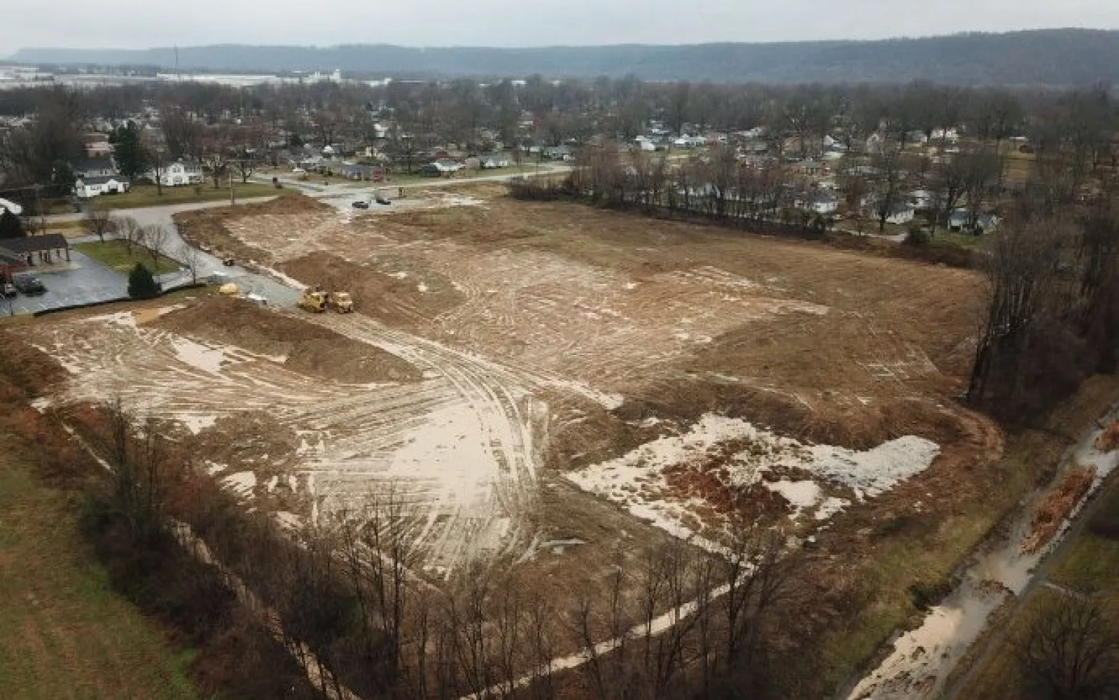 Cleared and leveled construction site with earthmoving equipment near residential area under cloudy sky