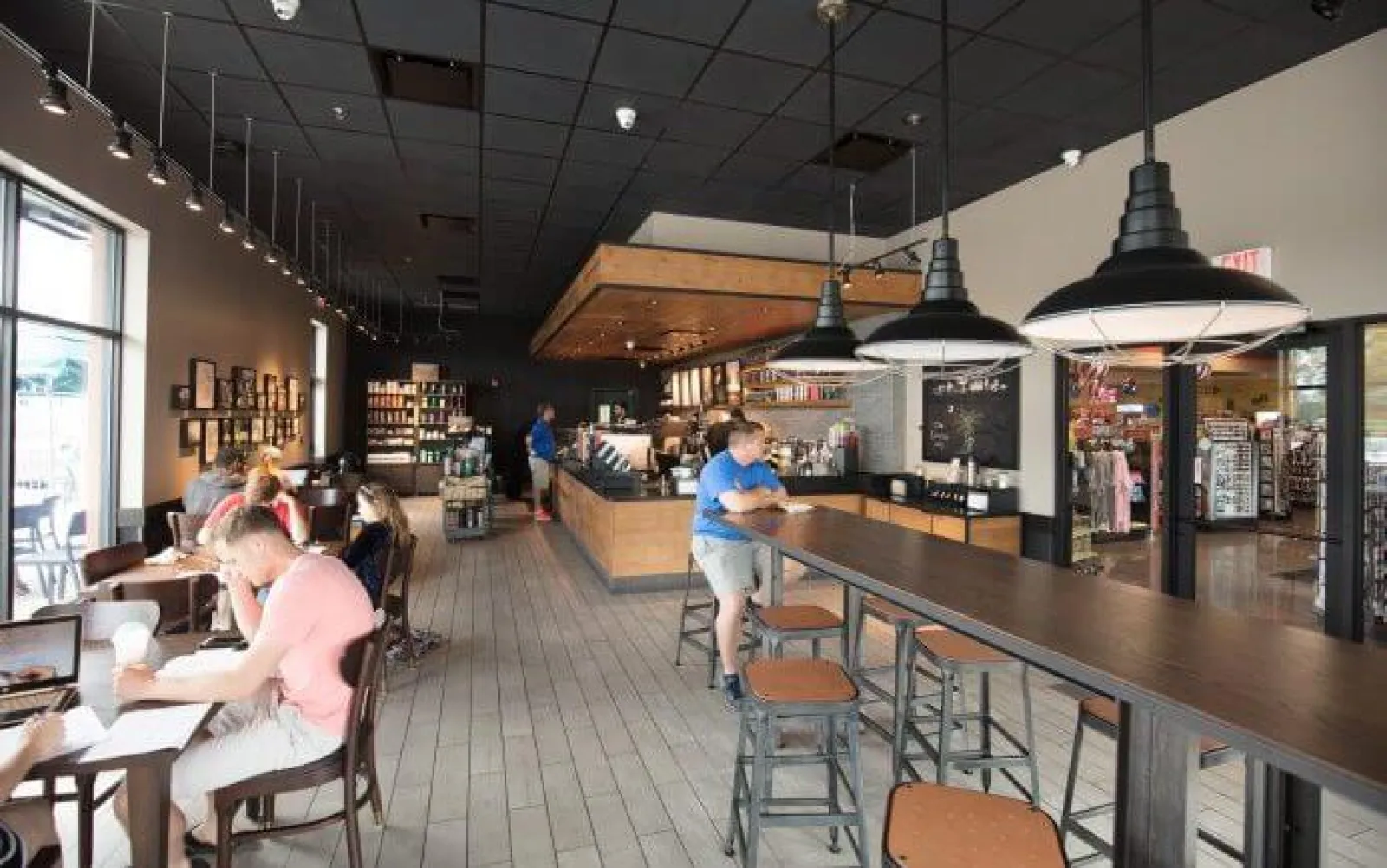 Modern coffee shop interior with wooden tables, pendant lights, customers working and ordering coffee.