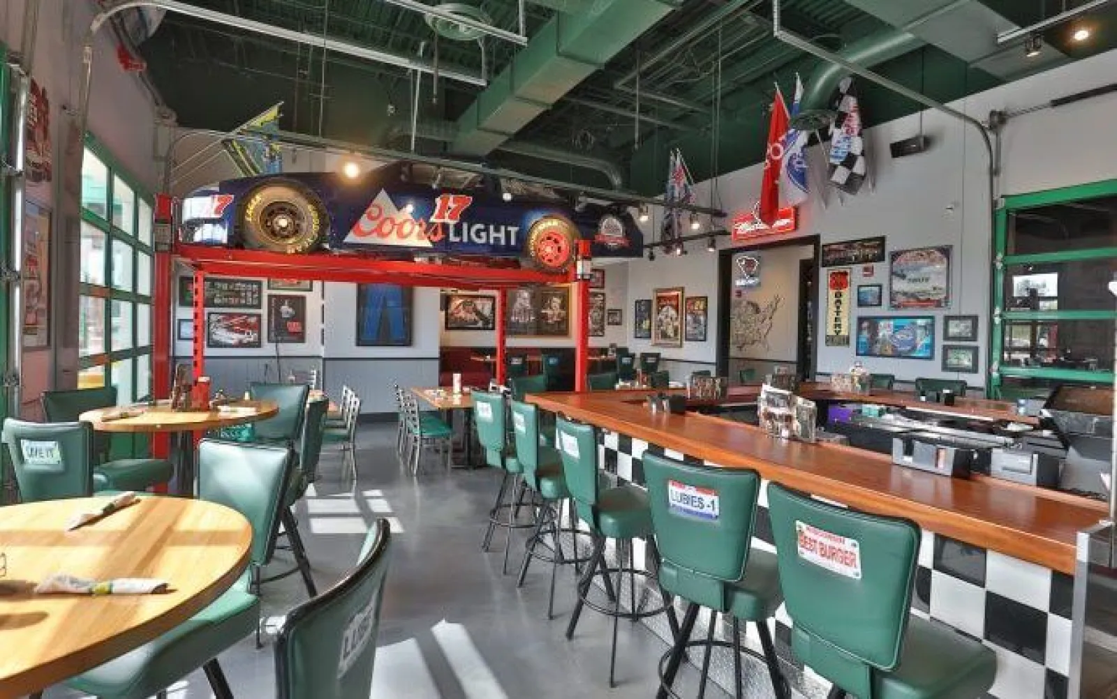 Retro diner interior with green chairs, wooden tables, racing memorabilia, and a Coors Light race car display.