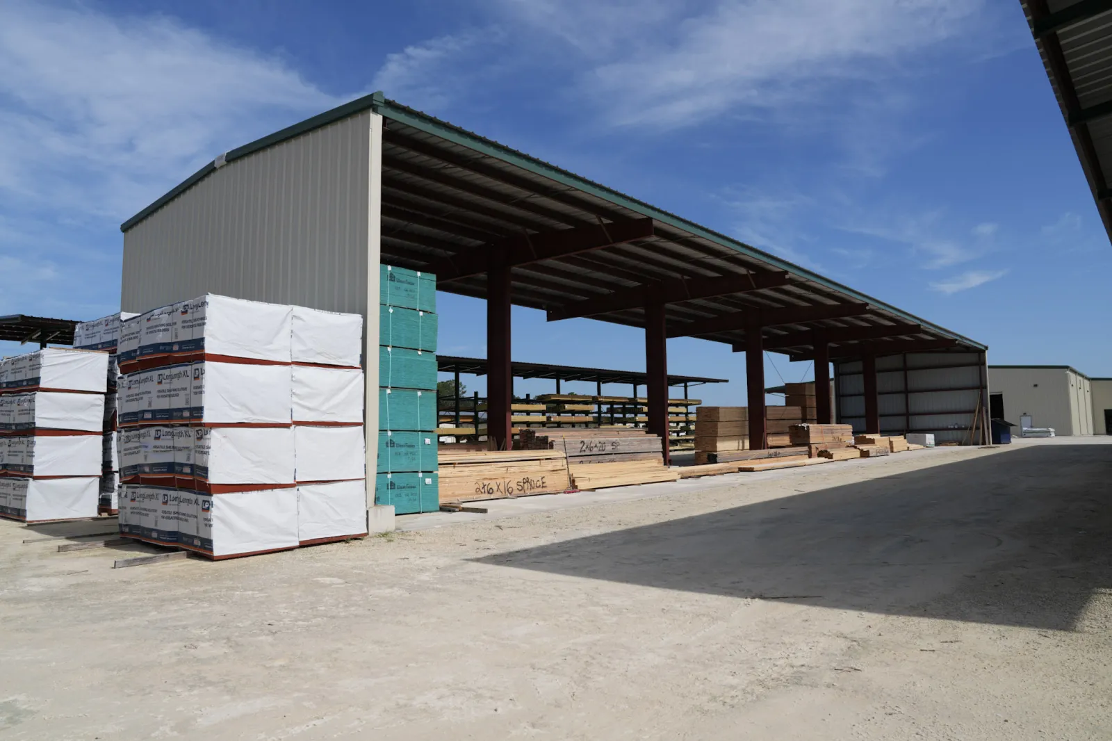 Outdoor lumber yard with stacks of wood and building materials under clear blue sky and metal shelter