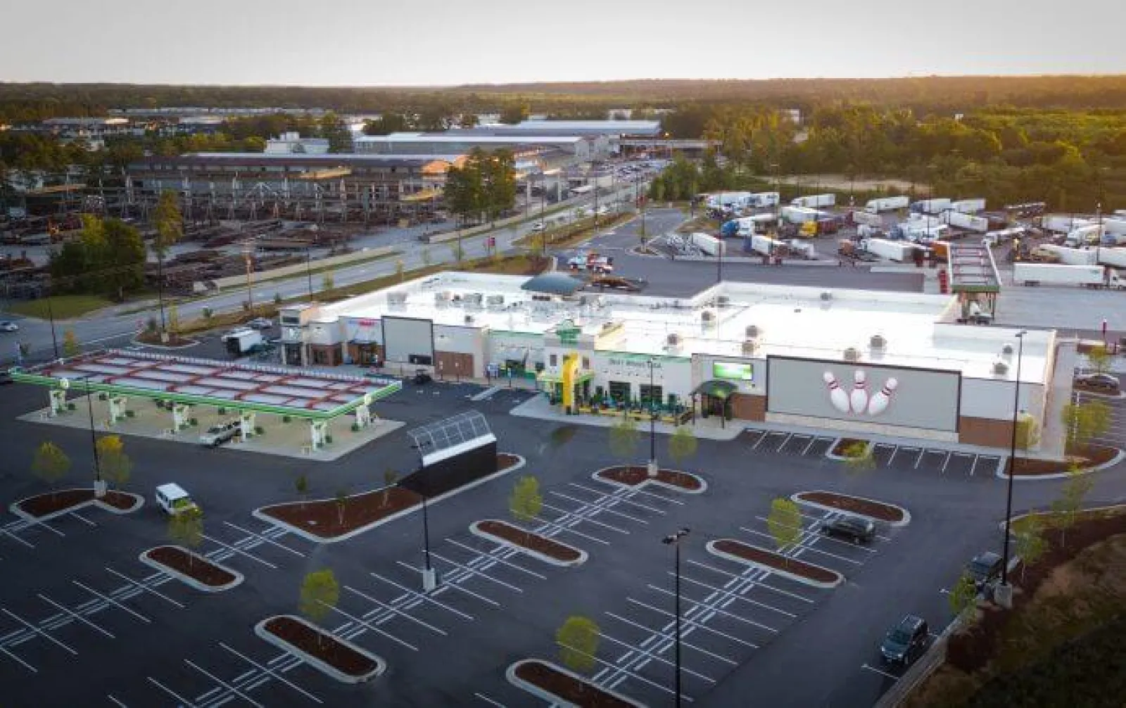 Aerial view of a commercial gas station with attached bowling alley and empty parking lot at sunset.