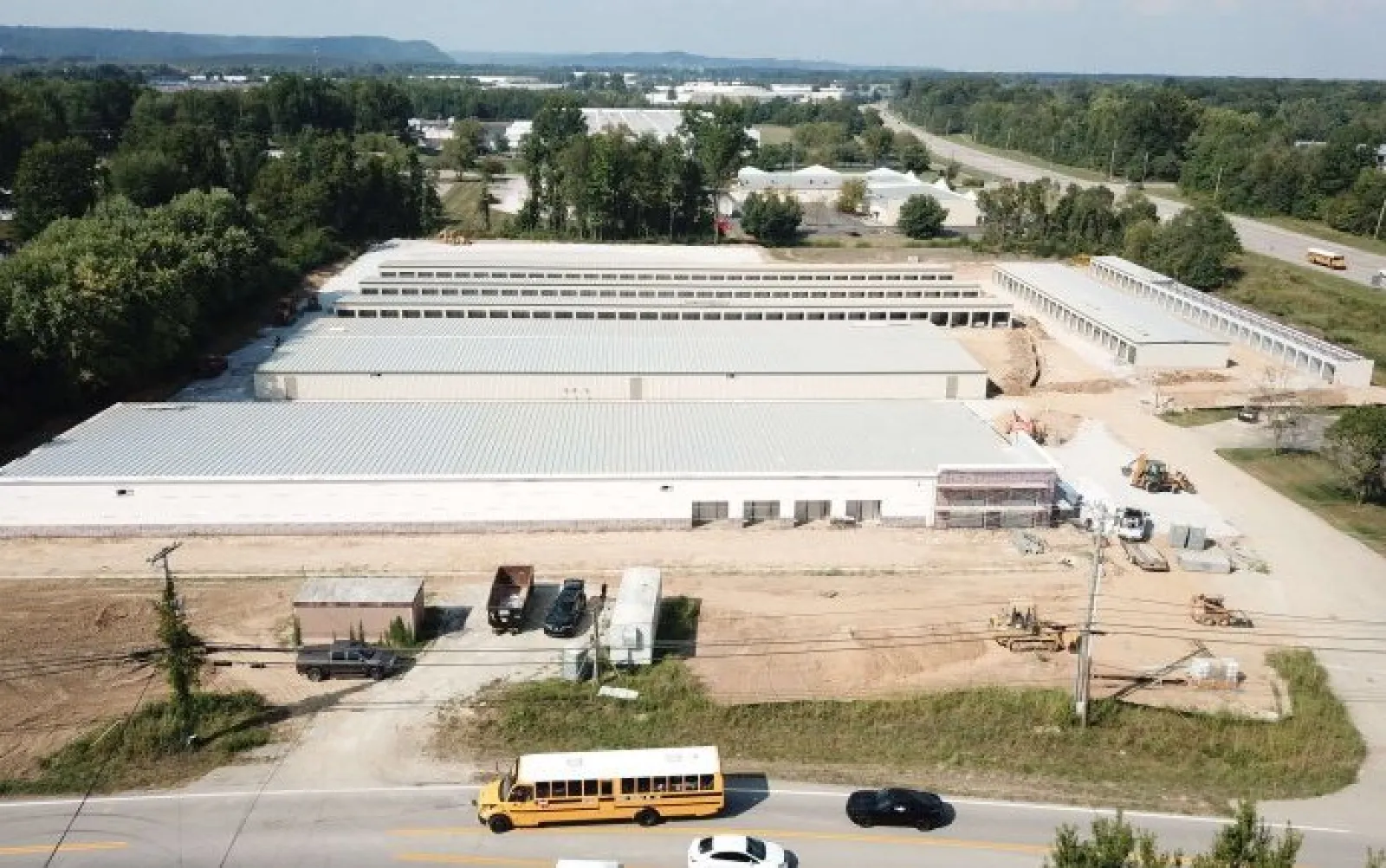 Aerial view of large industrial warehouses under construction with vehicles on adjacent road under clear sky