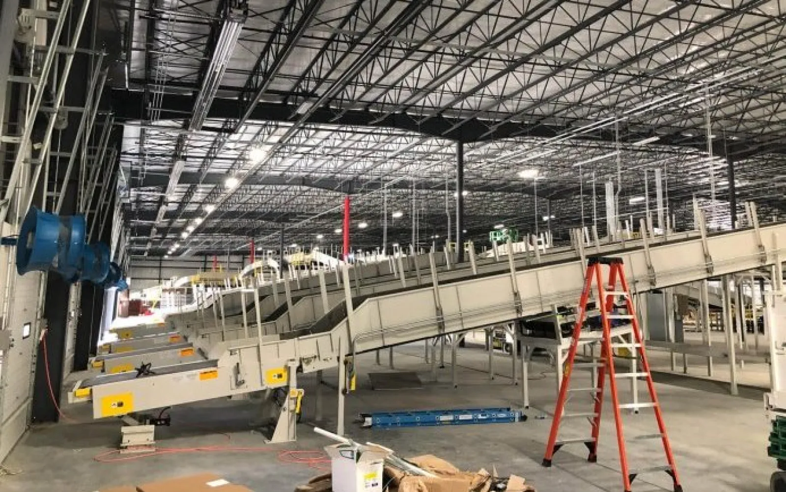Industrial conveyor belts and equipment under construction inside a large warehouse with high ceilings and exposed beams