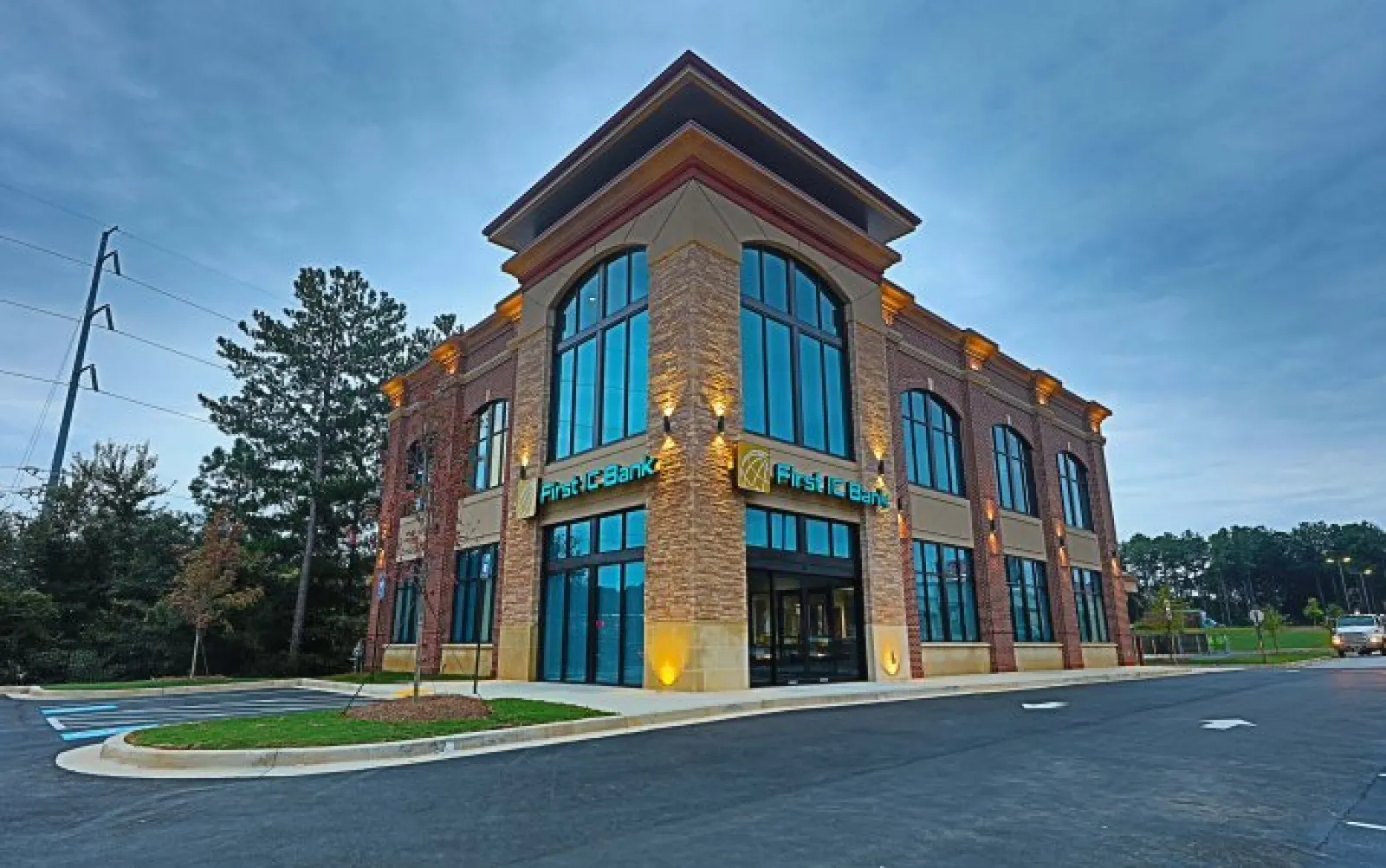 Modern two-story brick and glass First TC Bank building with parking and surrounding greenery at dusk.