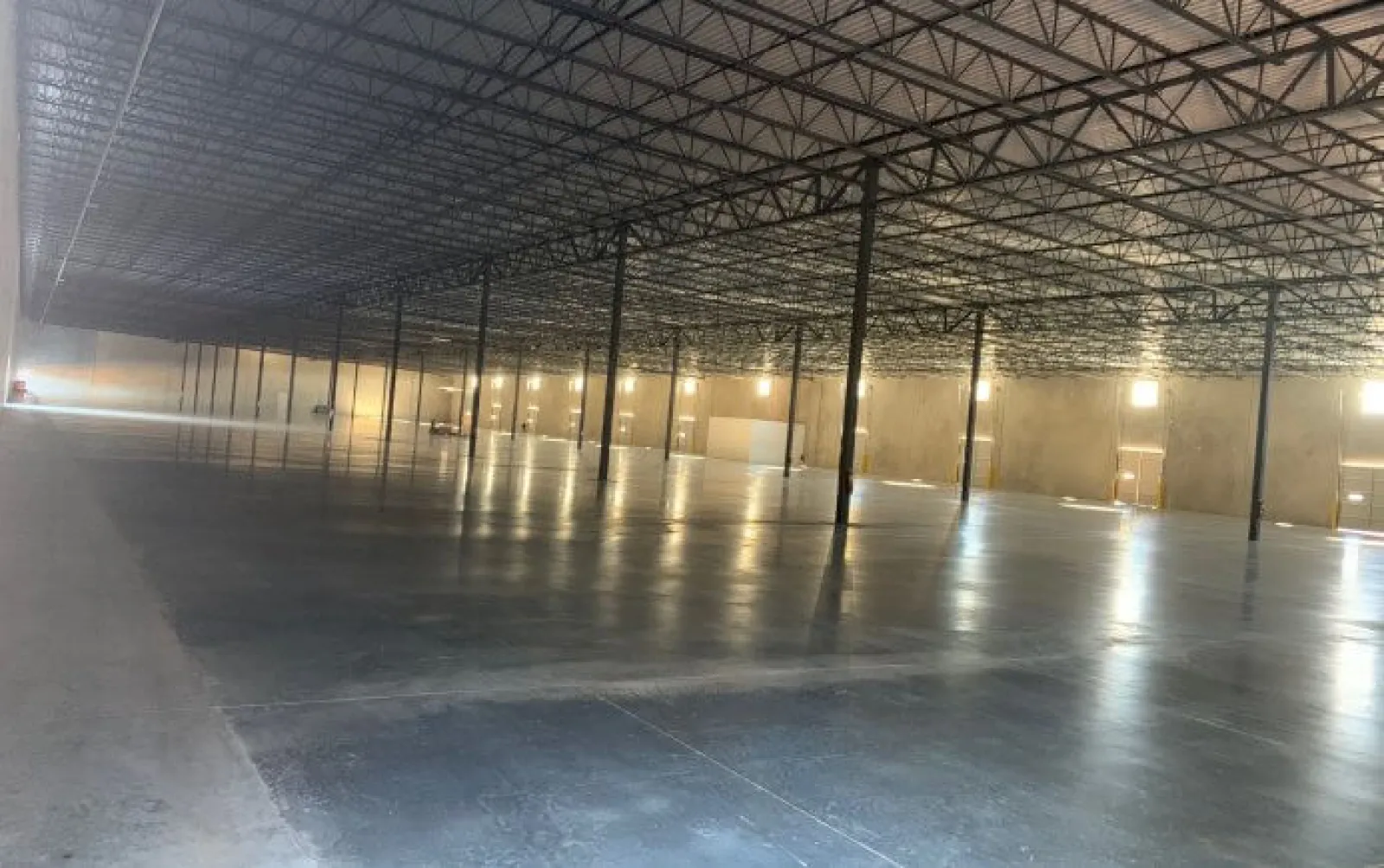 Spacious empty industrial warehouse with polished concrete floor, high ceiling, and metal support beams