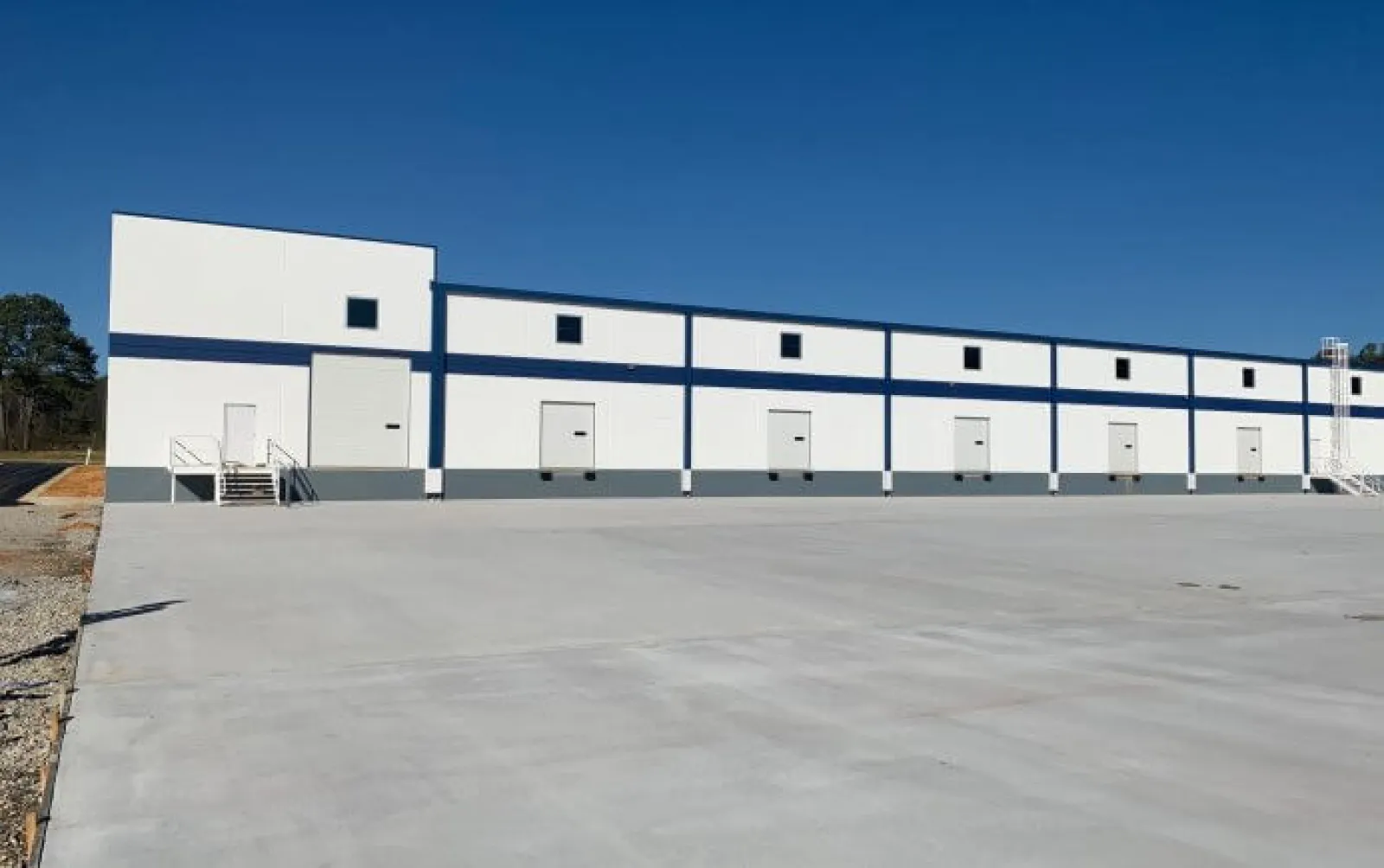 White and blue industrial warehouse with multiple loading dock doors under a clear blue sky