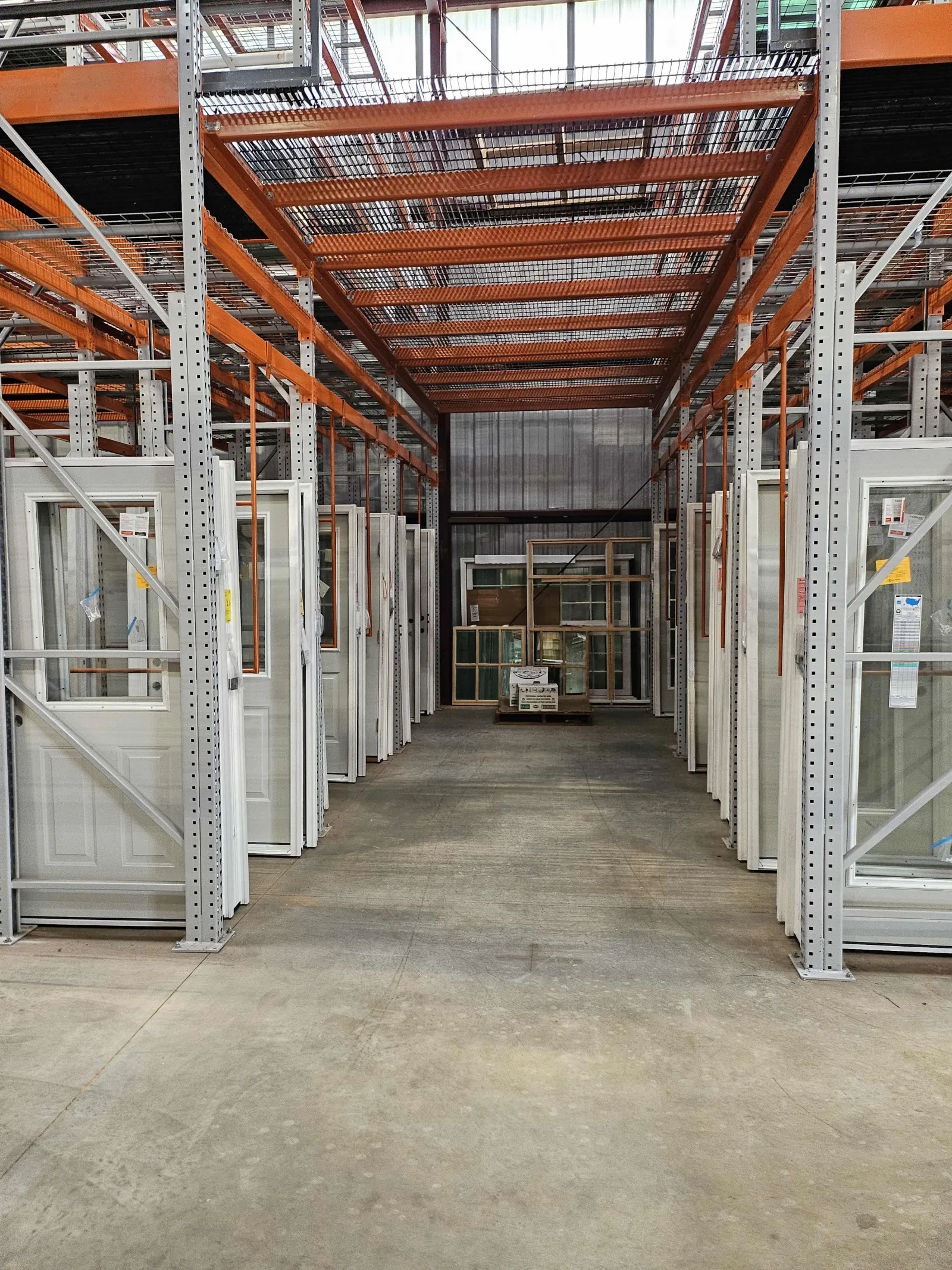Warehouse aisle with white framed doors and windows stored on metal racks with an orange overhead structure.