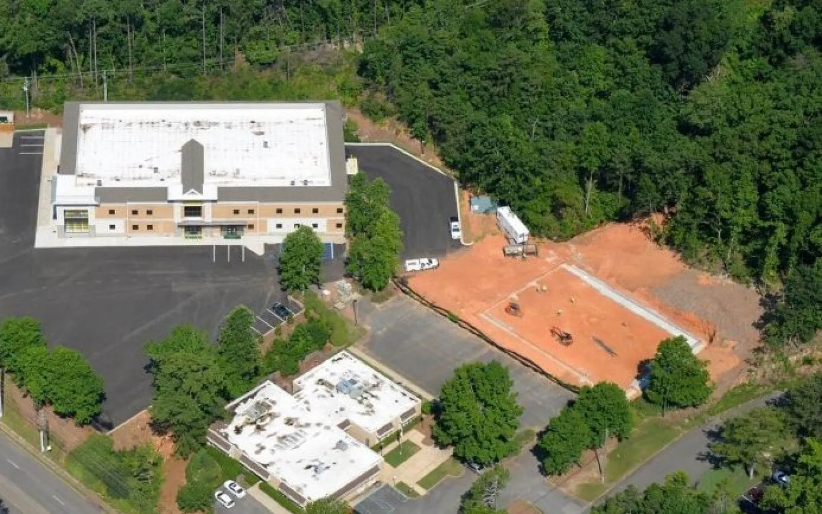 Aerial view of two commercial buildings beside a construction site surrounded by trees and parking lots.