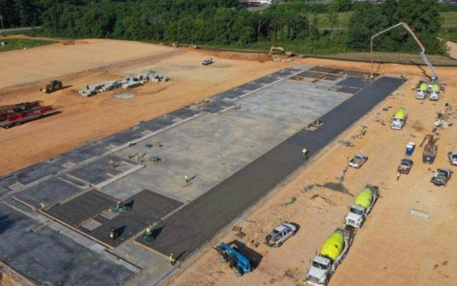 Aerial view of concrete foundation being poured at a large construction site with trucks and workers.