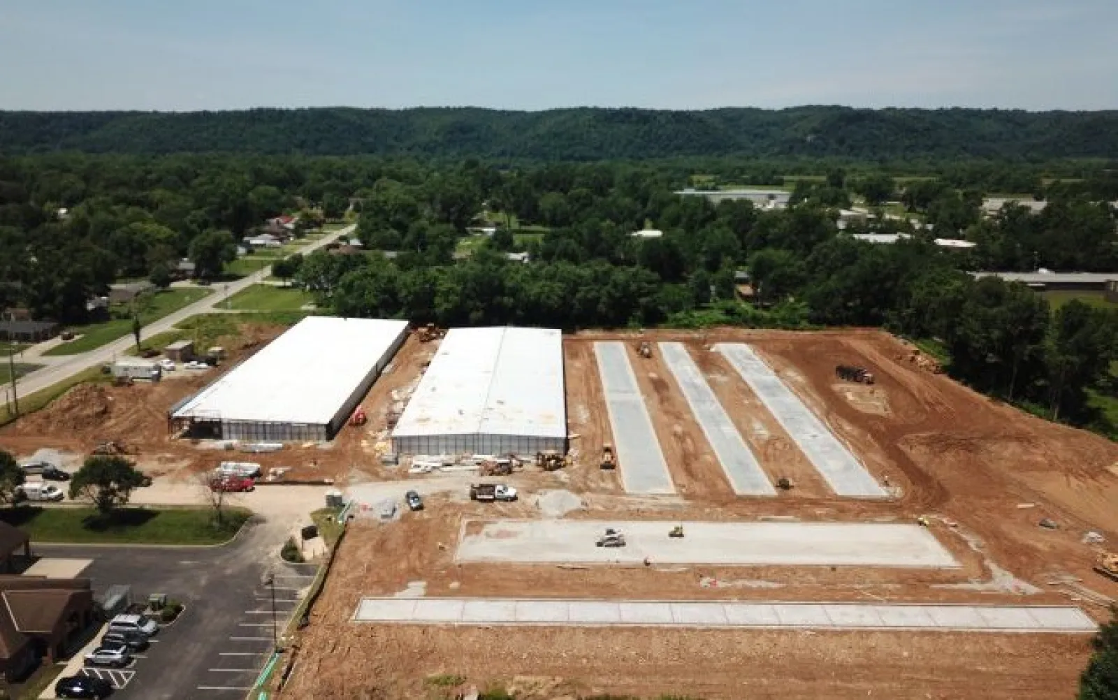 Aerial view of a construction site with two large warehouse buildings and concrete slabs surrounded by dirt and greenery.