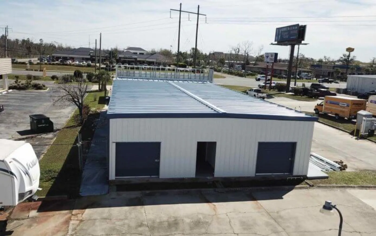 A white metal warehouse building with two large garage doors and an open entrance under a clear sky.
