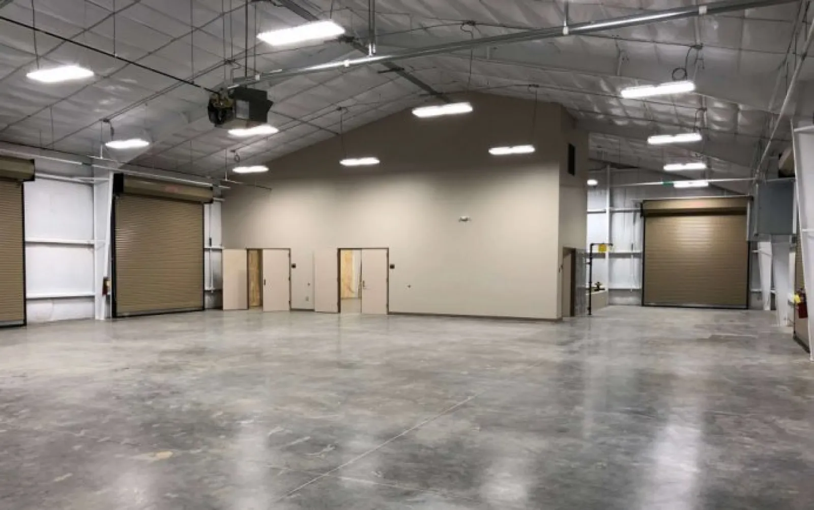 Spacious empty warehouse interior with polished concrete floor, high ceiling, and large roll-up doors.