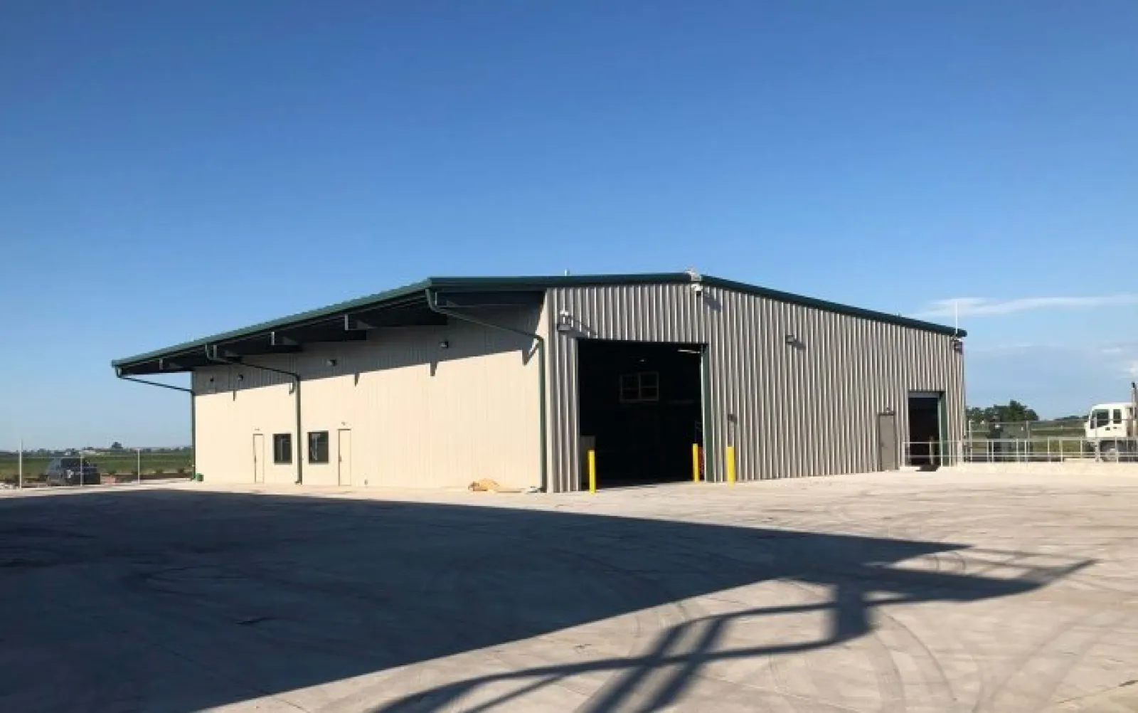 Large metal warehouse with beige and gray walls under a clear blue sky in an open paved area.