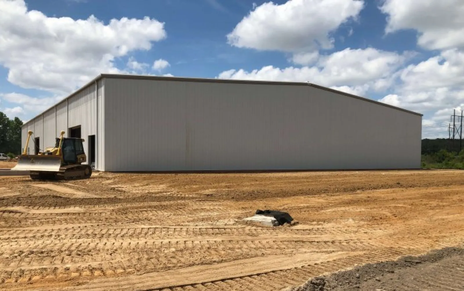 New large metal warehouse on construction site with bulldozer and clear blue sky with clouds