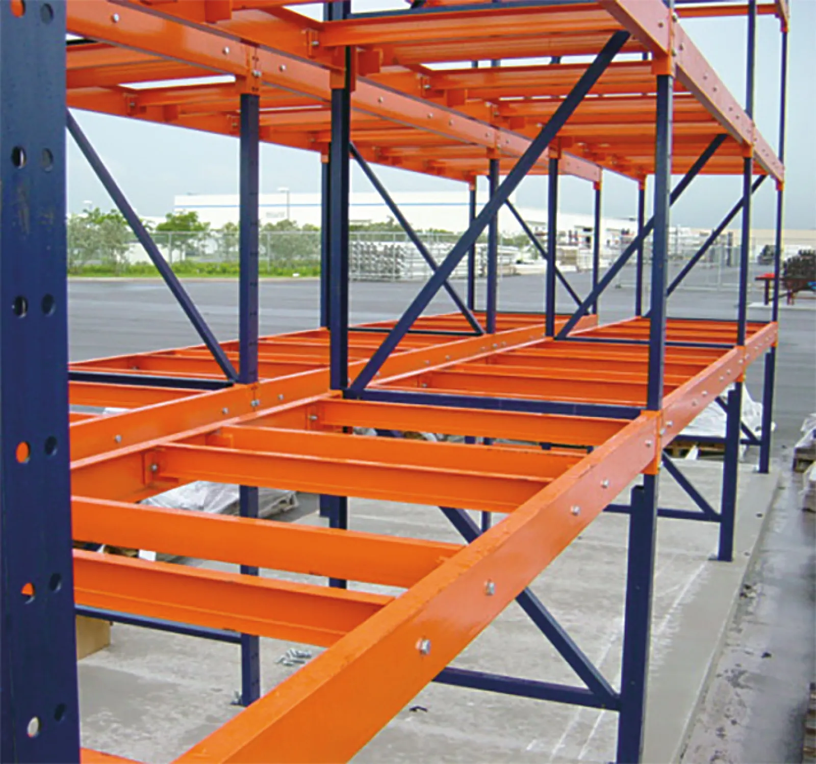 Orange and blue industrial metal storage rack shelving outdoors on concrete surface near warehouse.