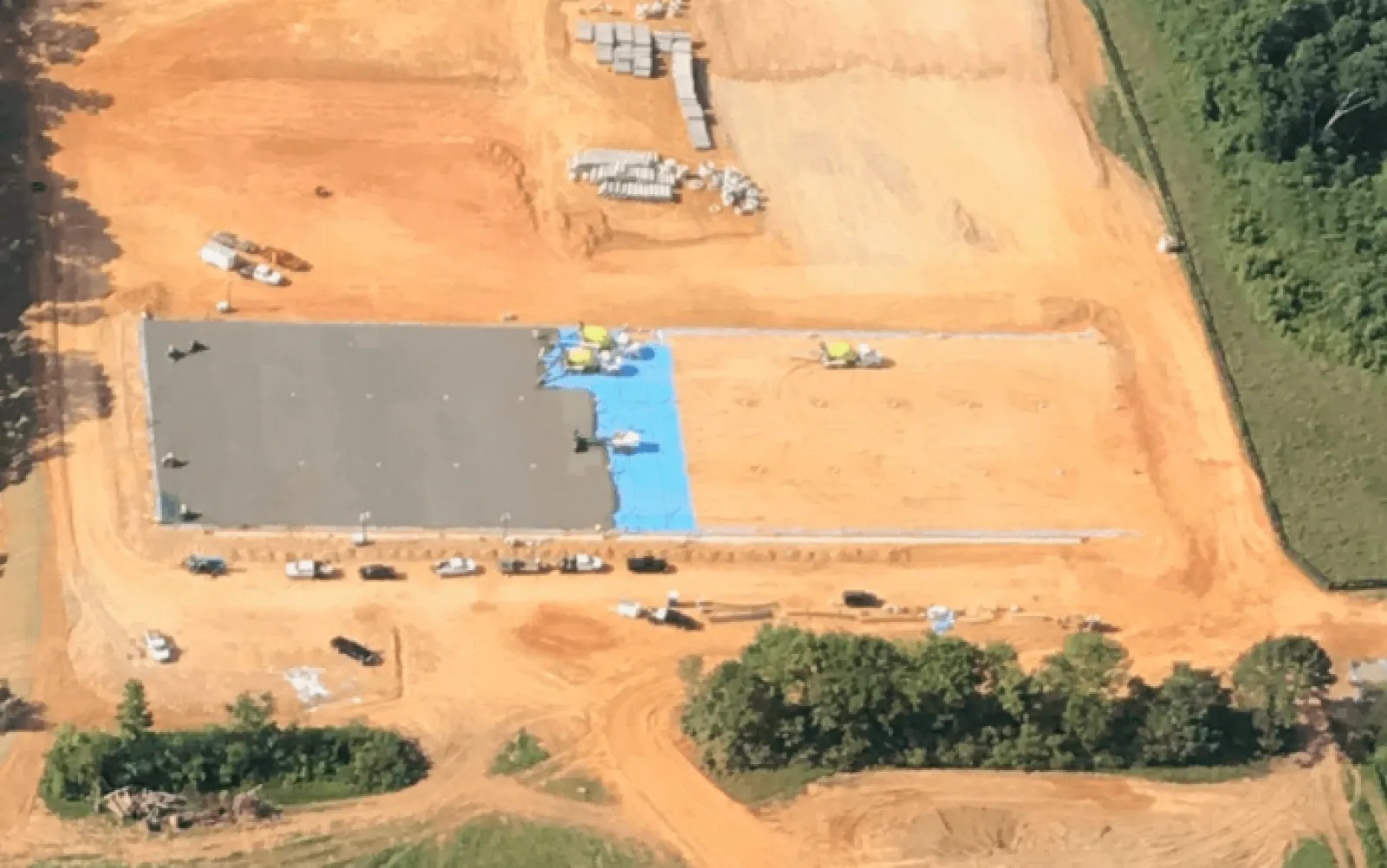 Aerial view of a large construction site with concrete foundation work and surrounding earth moving activities.