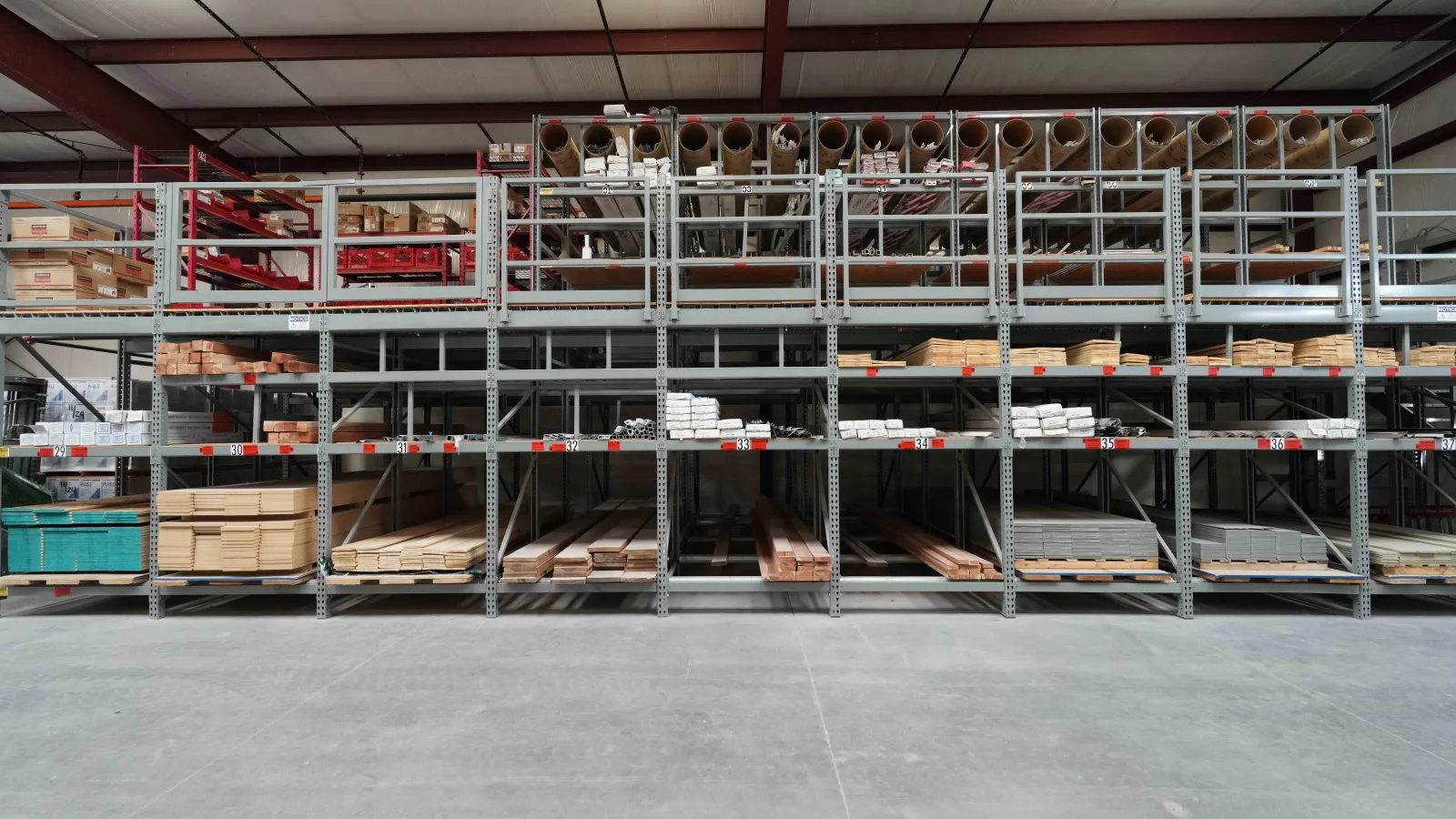 Organized warehouse shelves stocked with wood planks, pipes, and building materials in a large industrial space