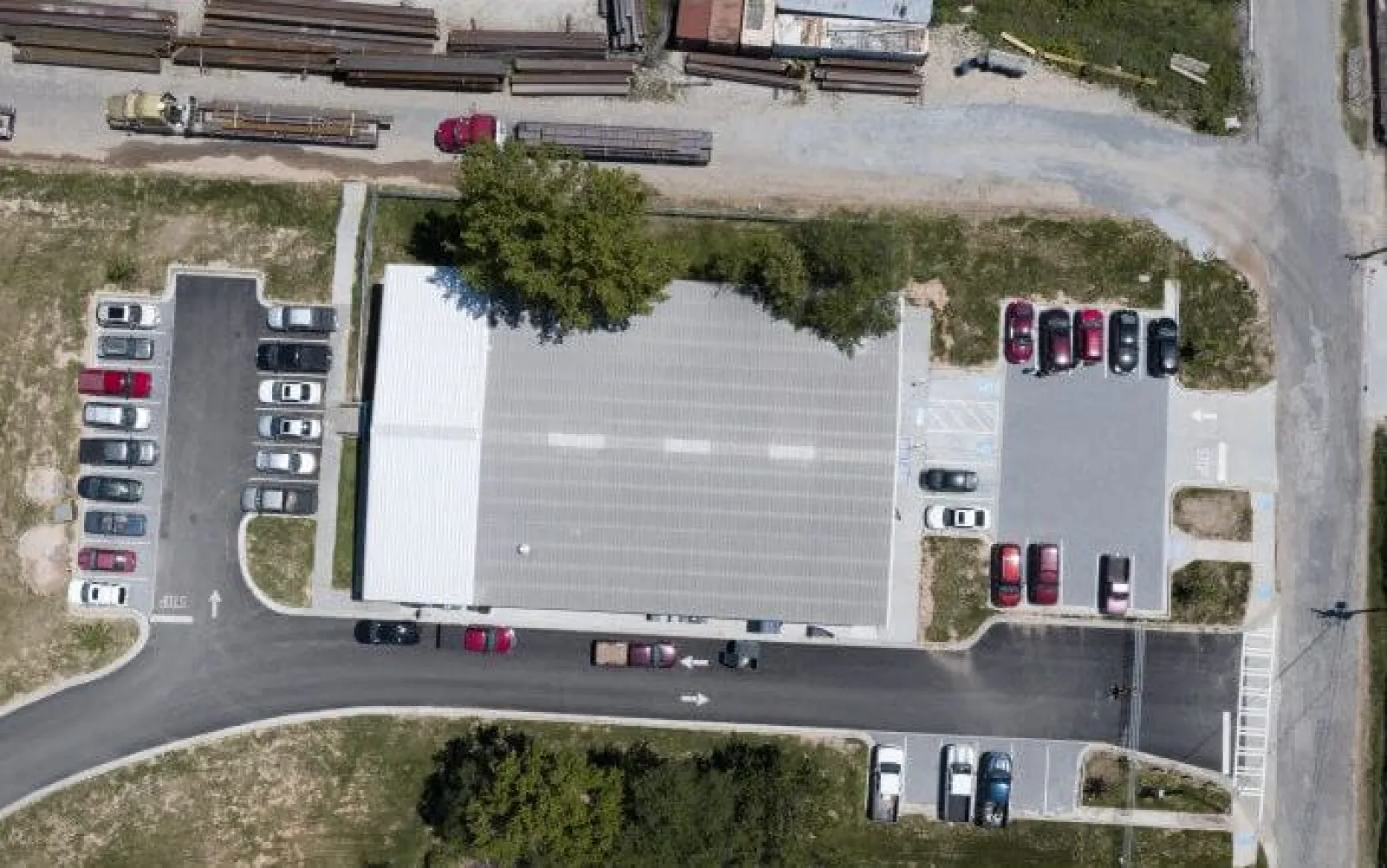 Aerial view of a commercial building with multiple parked cars and trucks surrounding it on paved roads.