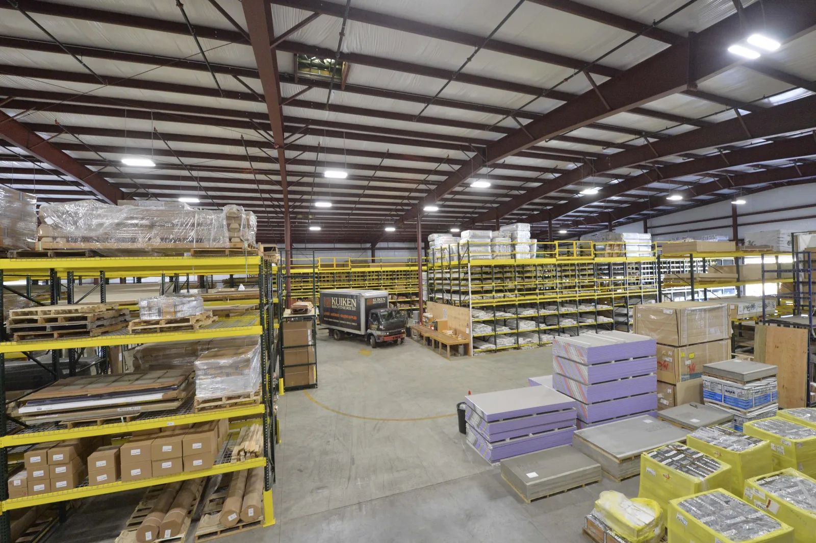 Spacious warehouse with metal racks, pallets, stacked boxes, and a delivery truck inside a large industrial building.