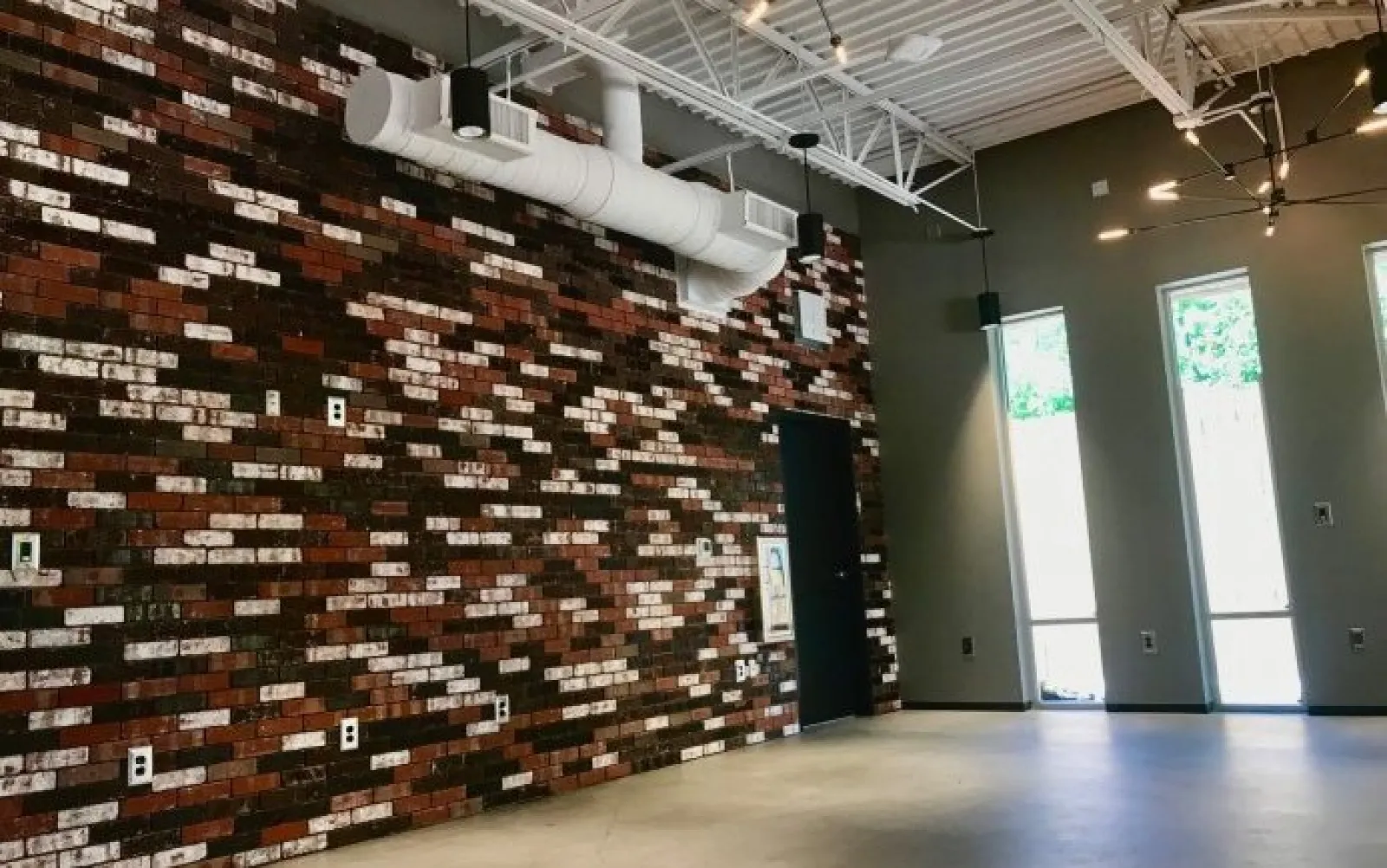 Industrial-style room with exposed brick wall, high ceiling, large windows, and concrete floor.