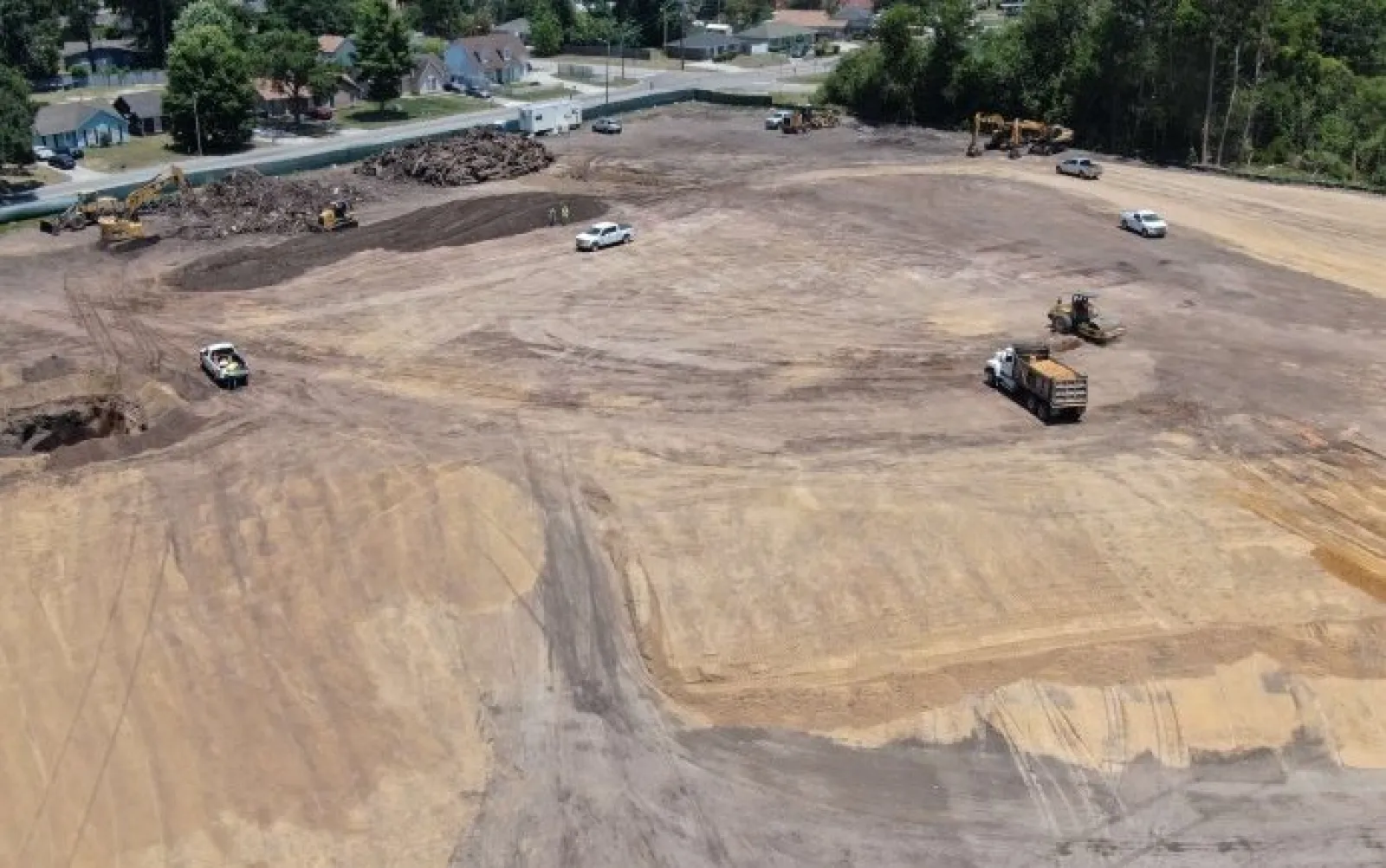 Aerial view of a large dirt construction site with machinery and trucks working on land clearing near a residential area