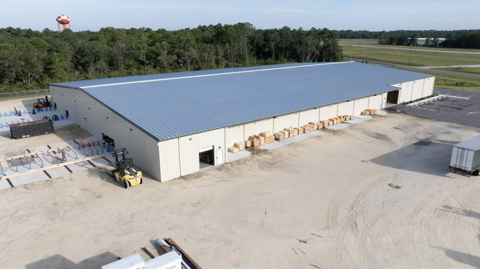 Aerial view of a large metal warehouse with a forklift and stacked pallets in a rural setting