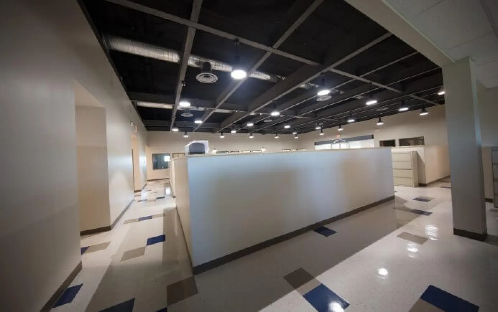 Modern empty office space with cubicles, polished floors, and overhead industrial lighting.