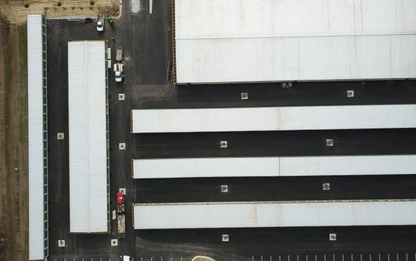 Aerial view of multiple long white-roofed warehouse buildings with black asphalt roads and parking areas.
