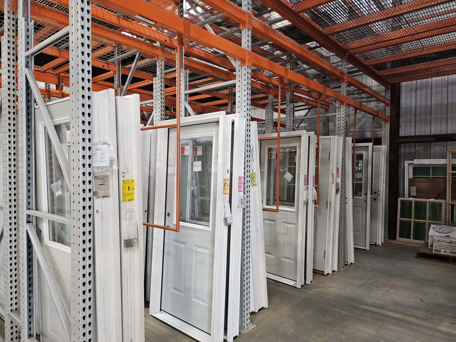 Rows of white doors with windows displayed on orange and gray metal racks inside a warehouse.
