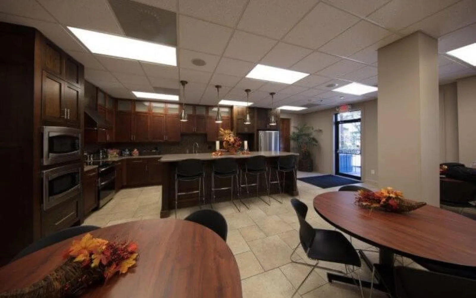 Modern kitchen and dining area with dark wood cabinets, island seating, and round tables with fall centerpieces.