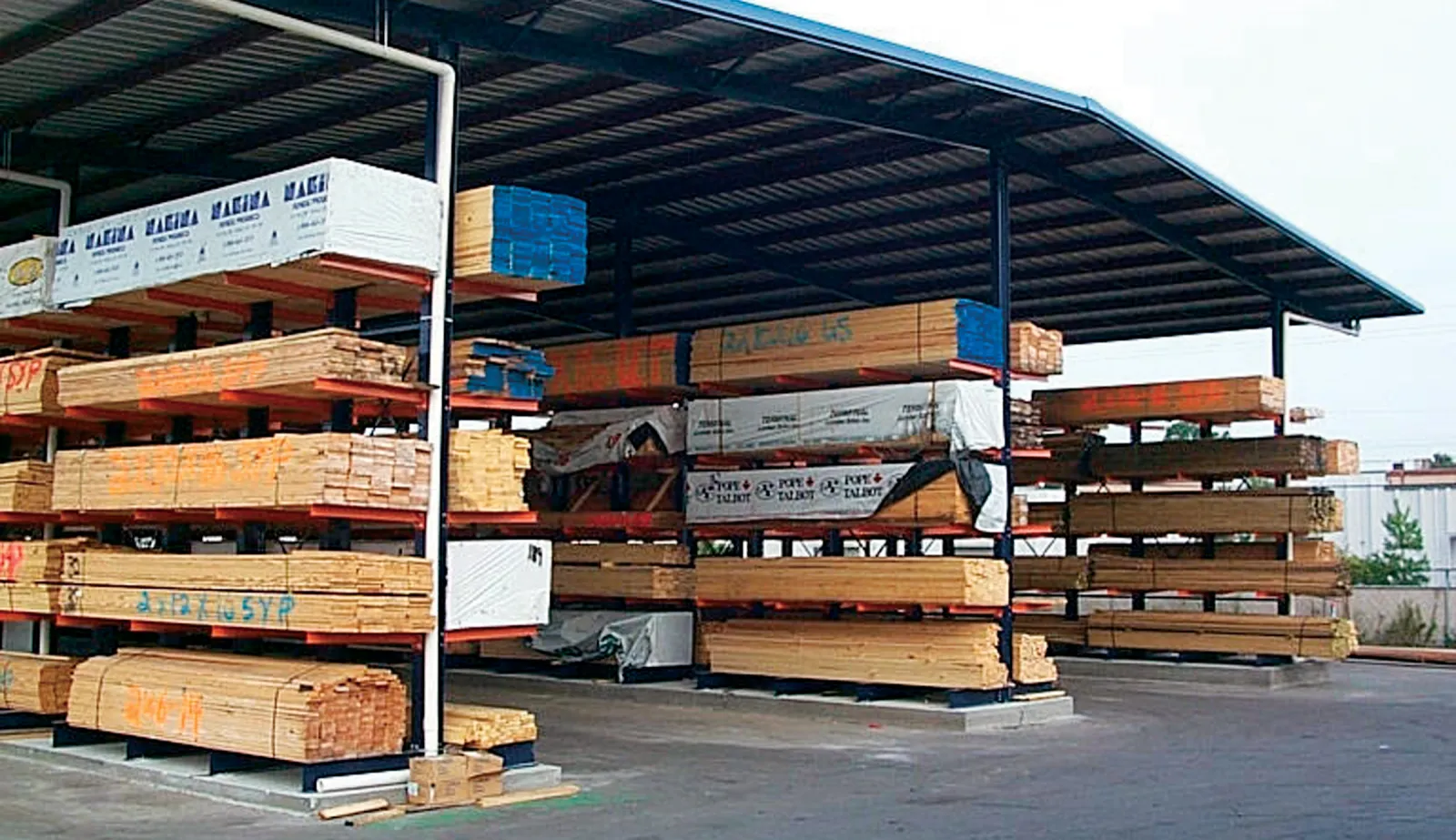 Covered outdoor lumber storage with multiple stacks of wooden planks organized on metal racks.