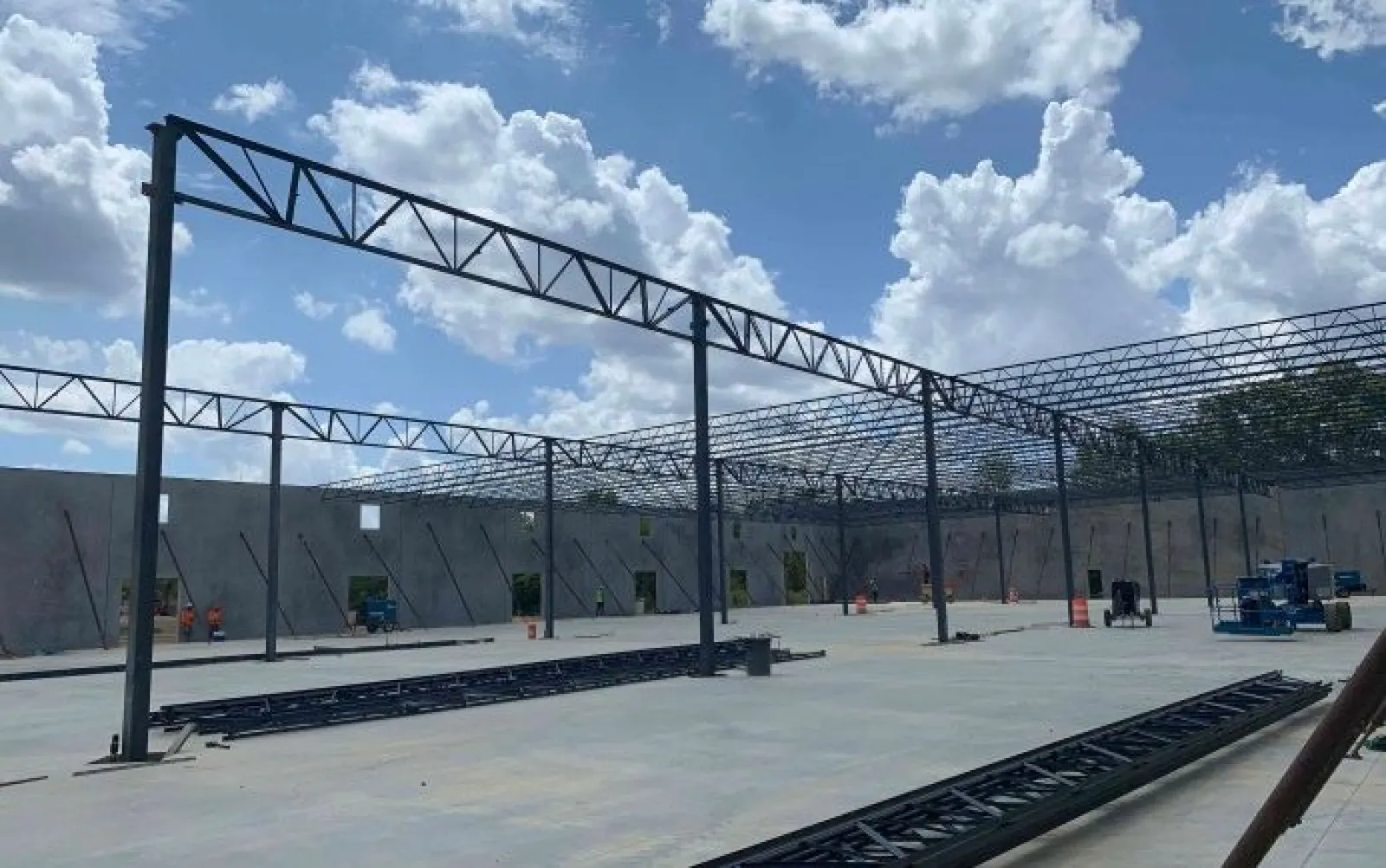 Steel framework construction in progress inside a large building under a cloudy blue sky.