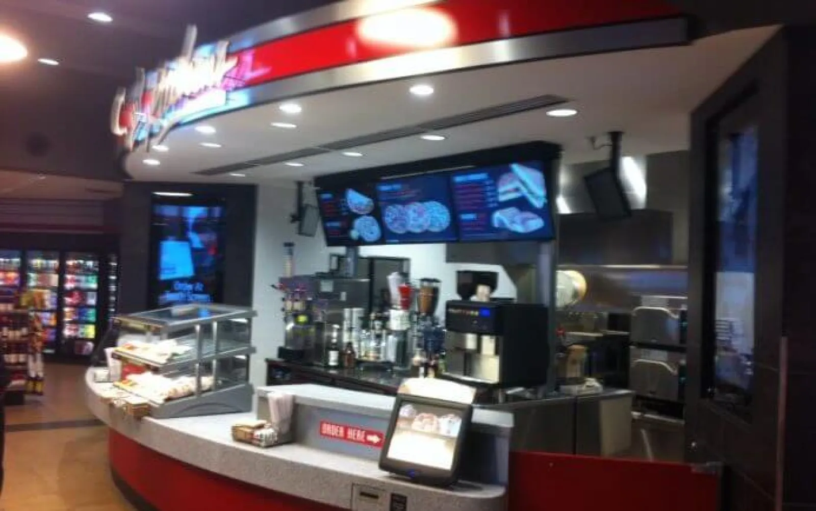 Modern fast food counter with digital menu screens and beverage machines inside a convenience store