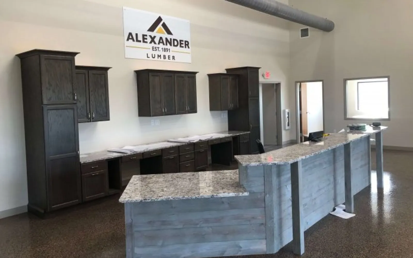 Modern office interior with granite countertop reception desk and dark wood cabinets under an Alexander Lumber sign.