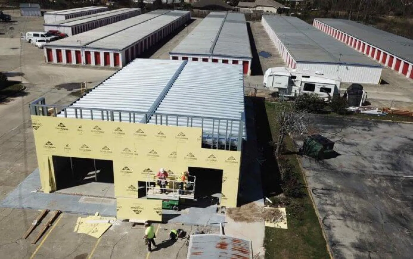 Construction workers building a prefab storage unit building near multiple storage units with red doors.