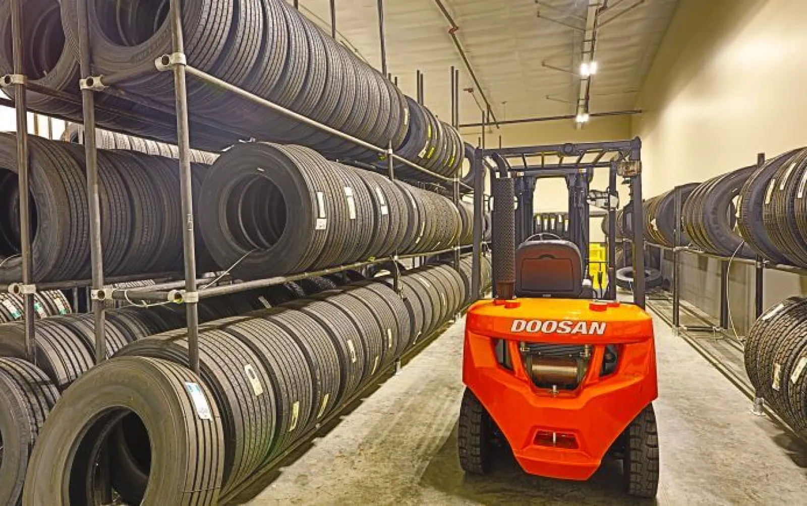 Red Doosan forklift in a warehouse aisle surrounded by shelves stacked with black tires