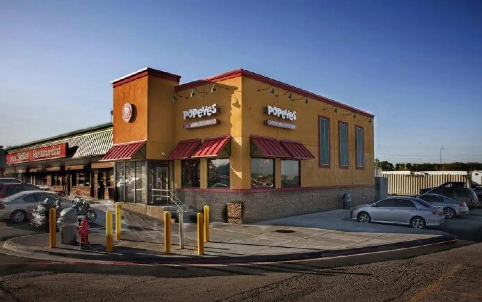 Popeyes Louisiana Kitchen restaurant building with cars parked outside on a clear day.