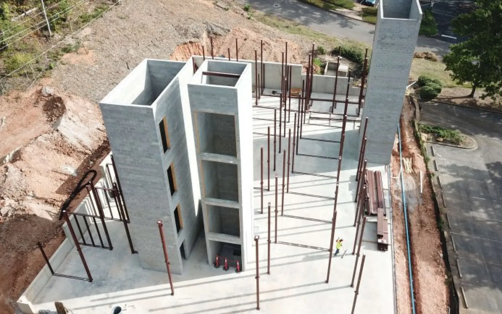 Aerial view of gray concrete building under construction with exposed steel beams and workers onsite.