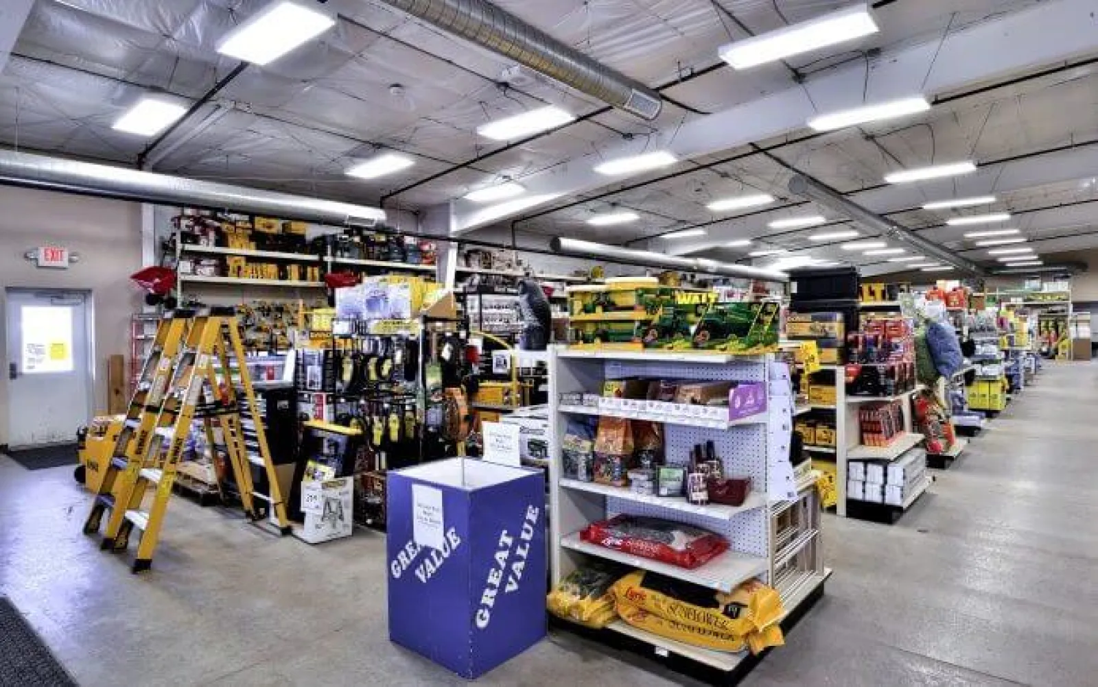Bright hardware store interior with ladders, shelves stocked with tools, pet food, and various home improvement items.