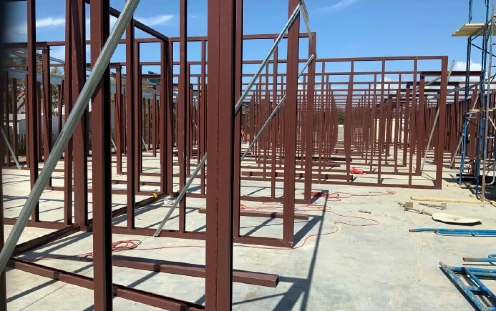 Steel framework structure under construction on concrete floor with clear blue sky background.