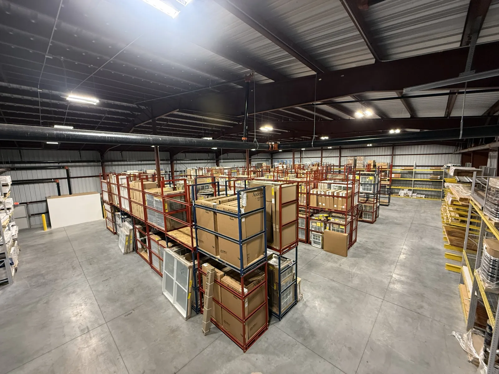 Spacious warehouse with metal shelving racks storing boxed inventory and building materials under bright ceiling lights