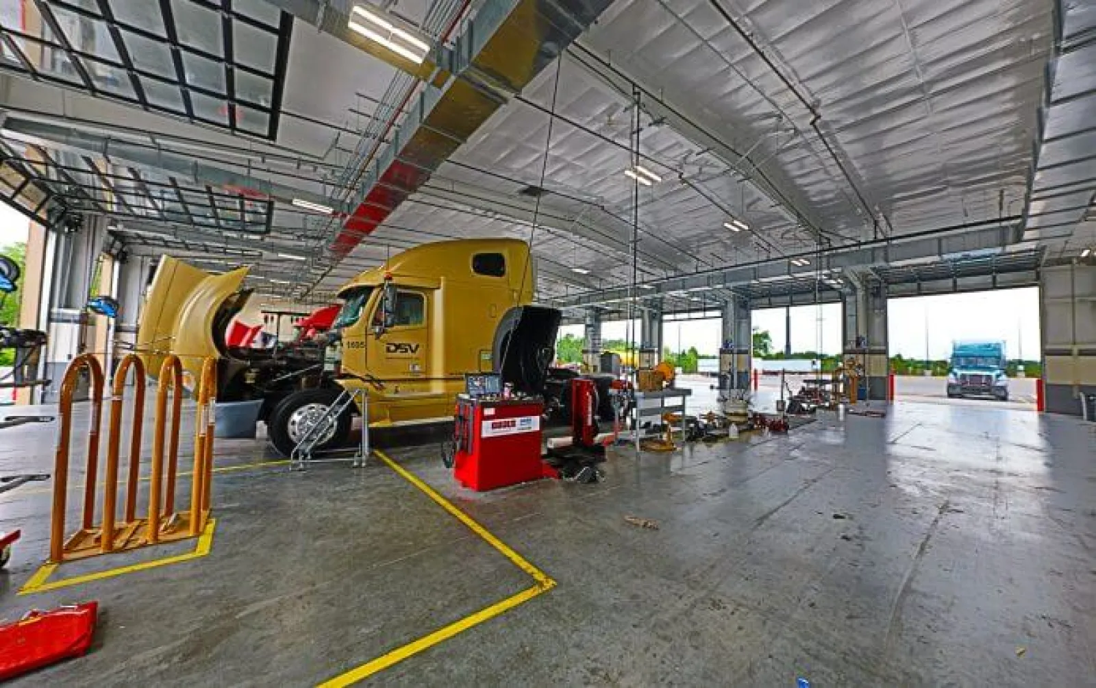 Interior of a large truck maintenance garage with a yellow semi truck being serviced under bright lighting.