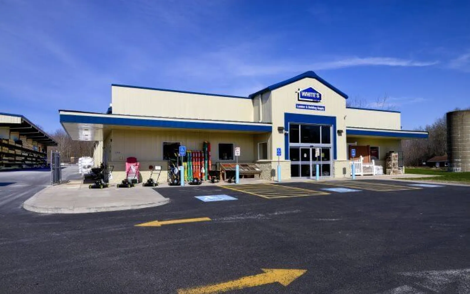 Exterior view of White's Lumber and Building Supply store with equipment and handicap parking under a clear blue sky.