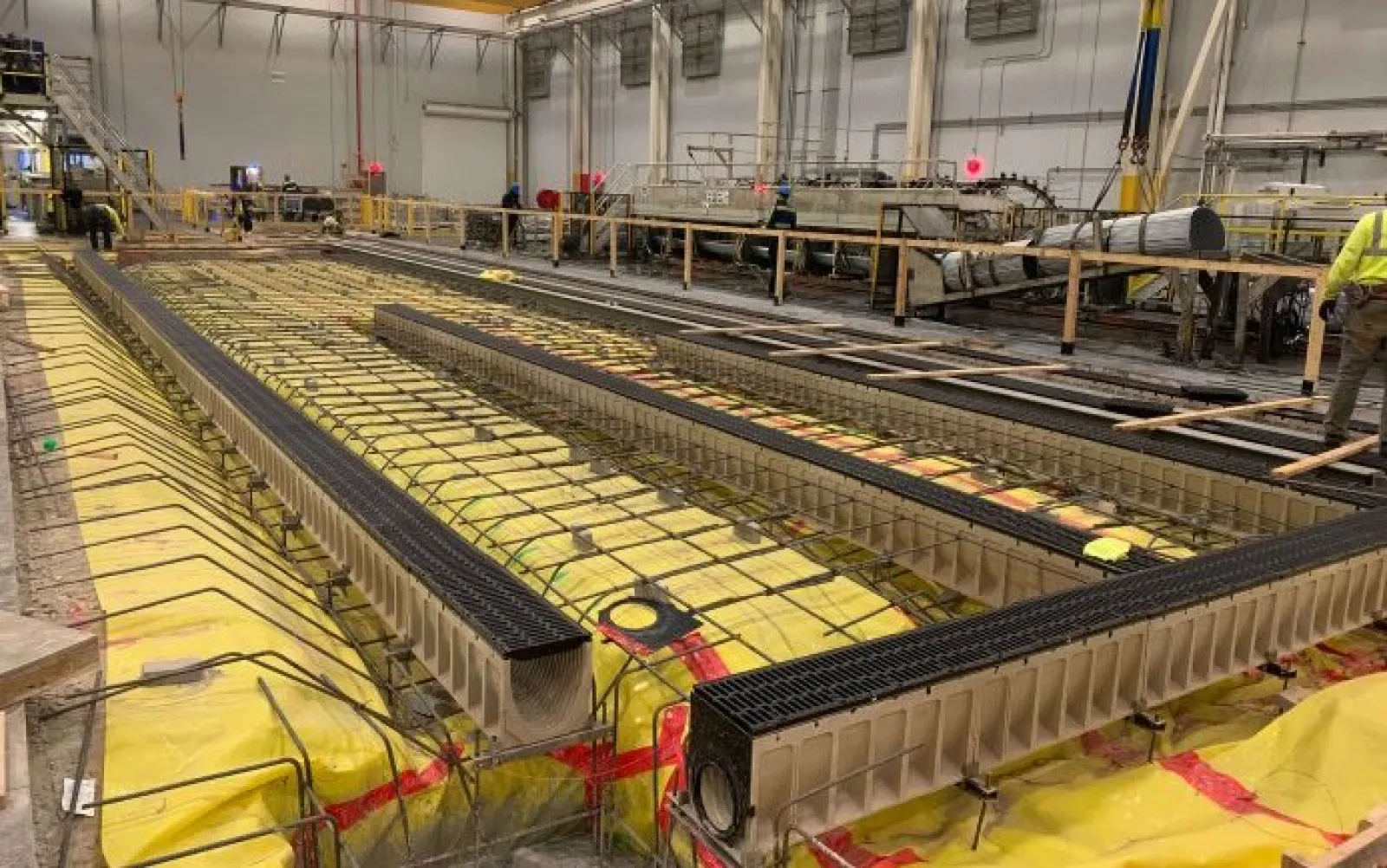 Indoor construction site with insulated trenches and steel reinforcements for concrete pouring in progress.