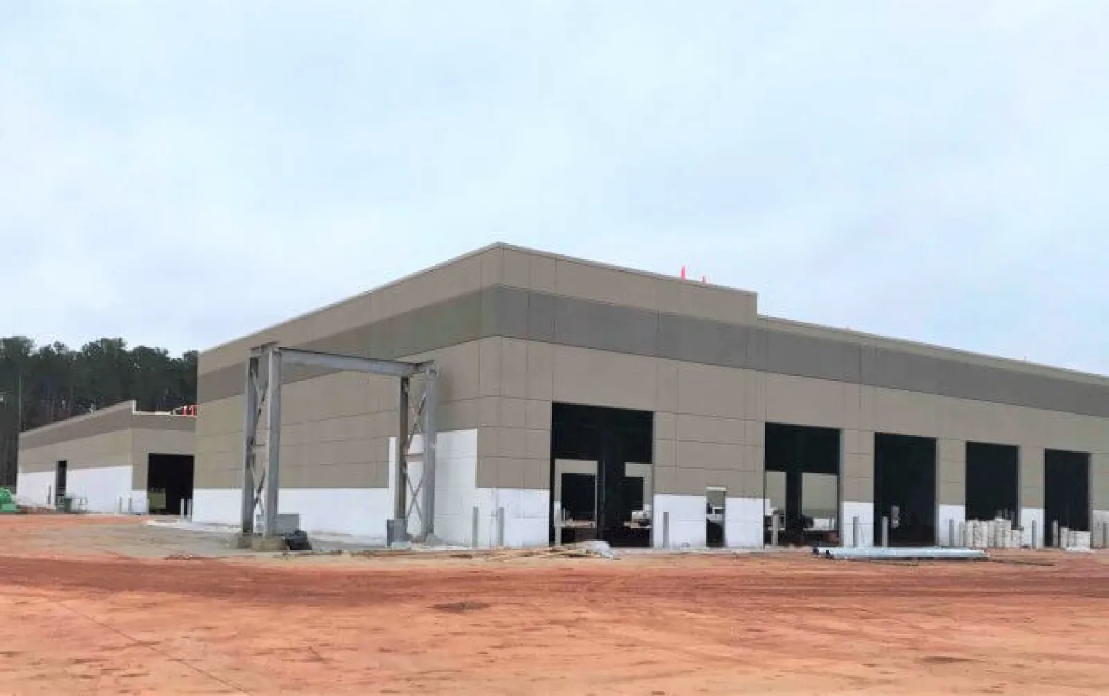 Large industrial warehouse building under construction with multiple loading dock doors and red soil ground.
