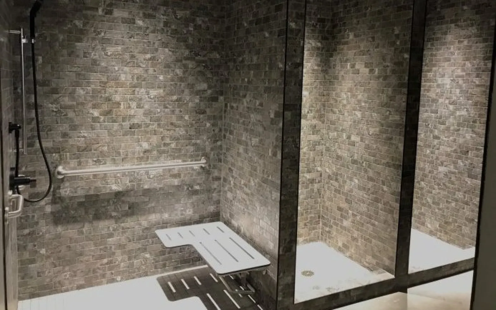 Accessible shower with foldable seat, grab bar, and dark tiled walls in a modern bathroom space.