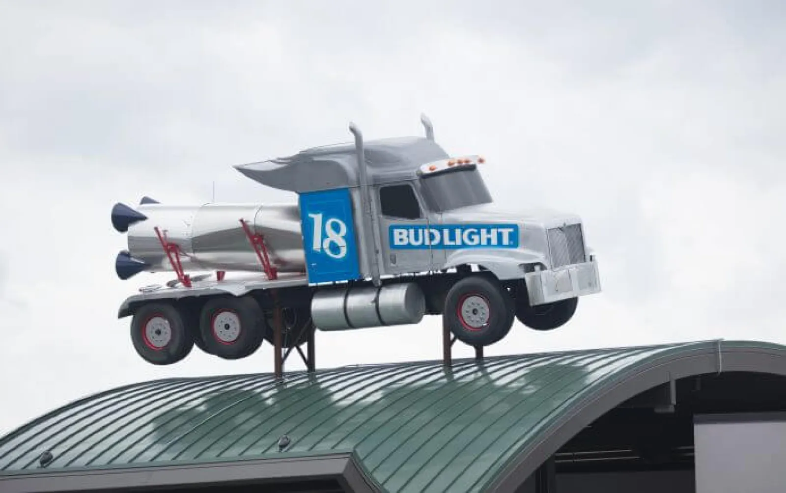 Silver Bud Light truck with rocket detail mounted on a curved green rooftop against a gray sky.