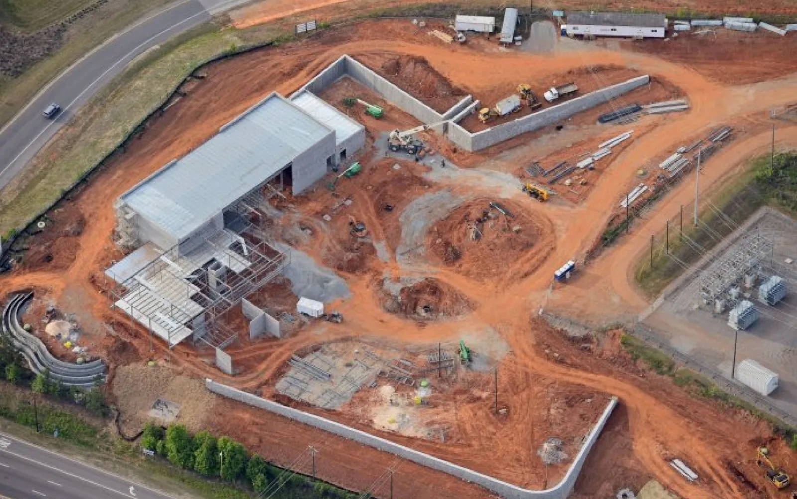 Aerial view of a construction site with a partially completed building and surrounding red earth roads
